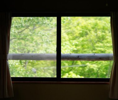 View of lush trees through framed window with curtains at Piporo Norikura in Nagano