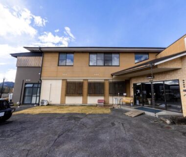 Two-story ryokan exterior with entrance, parking area and distant mountains in Gifu