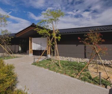 Low single-story ryokan entrance with pathway, noren curtain and landscaped courtyard at 一 能登島 hitotsu notojima Ishikawa Japan