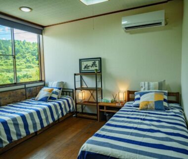 Twin beds with striped linens, wooden floor, large window view at Ichishuku Ikkei Isshōen, Ichihara, Chiba