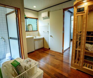 Interior wash area with wooden sauna cabinet, sink, shower stall and laundry basket at Ichishuku Ikkei Isshōen Chiba
