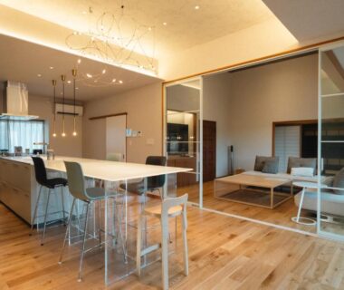 Spacious open-plan living area with kitchen island, bar stools, wood floors and glass partition to lounge