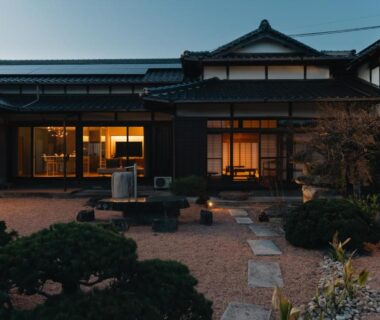 Evening exterior of a traditional Japanese ryokan with lit wooden facades, stone pathway and small garden in Ōita, Kyūshū