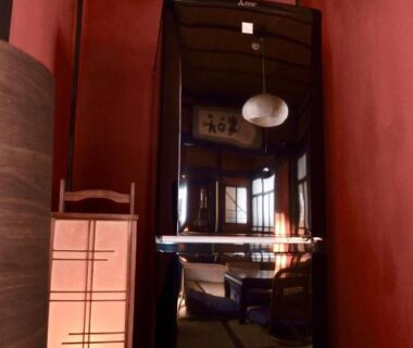 Narrow entrance with tall mirror, red walls, shoji lantern and pendant light inside Kabukiya guesthouse