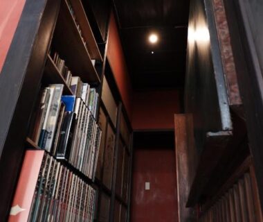 Narrow wooden corridor with bookshelf at 一棟貸ゲストハウス 傾㐂屋 Kabukiya in Hiroshima