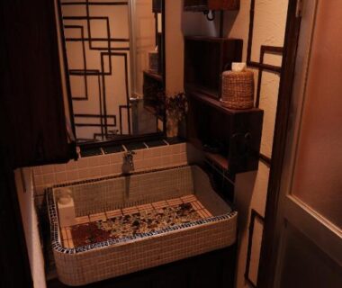 Mosaic-tiled wash basin and wooden cabinetry in a compact traditional ryokan interior at Kabukiya Hiroshima