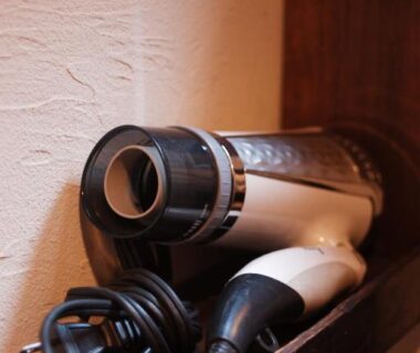 Compact hair dryer with cord on wooden shelf against textured plaster wall in ryokan room