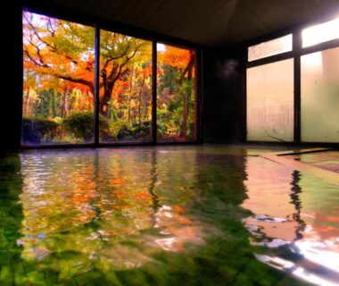 Indoor onsen bath overlooking autumn garden through large glass panels at Ichisui-sō, Niigata