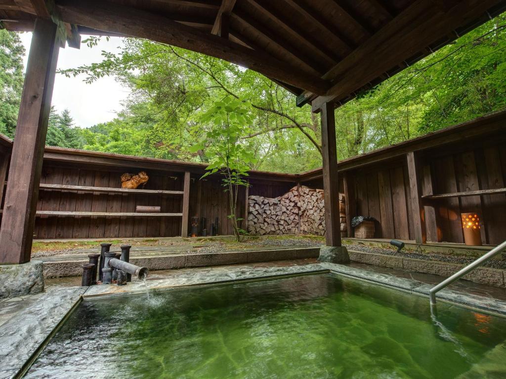 Outdoor Onsen Bath Ichisui-sō Niigata Japan Covered outdoor onsen with green mineral water, wooden bath and stacked firewood at Ichisui-sō, Niigata