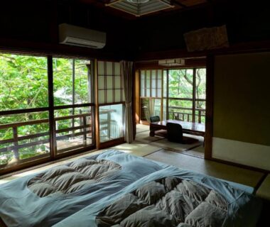 Traditional tatami room with futon bedding and shoji screens overlooking green foliage at Nakadana-sō, Nagano