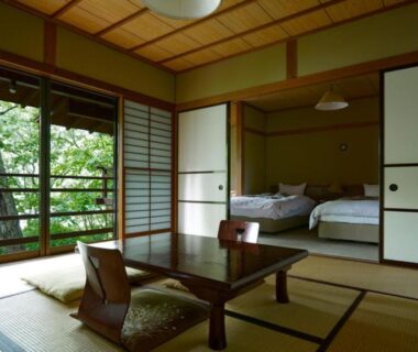 Traditional tatami room with low table, zabuton cushions, shoji screens and futons visible through sliding doors facing garden