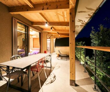 Covered wooden terrace at night with dining table, chairs and sliding glass doors overlooking trees at 五氣里-itsukiri- Chiba