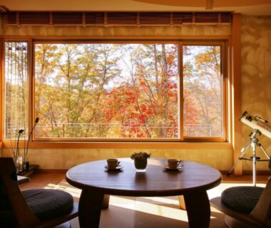 Tatami room with round low table, chairs, telescope and window framing autumn foliage at Ryokusuitei Sendai Akiu Onsen