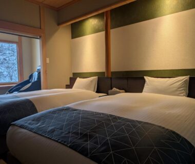 Two beds in a calm tatami room with window and wooden accents at Shinobu Onsen Seishū, Fukushima