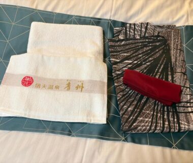 Folded patterned yukata, red obi and embroidered towels arranged on a bed at Shinobu Onsen Seishū in Fukushima