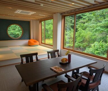 Tatami room with low dining table, circular window and lush forest view at Shinobu Onsen Seishū, Fukushima