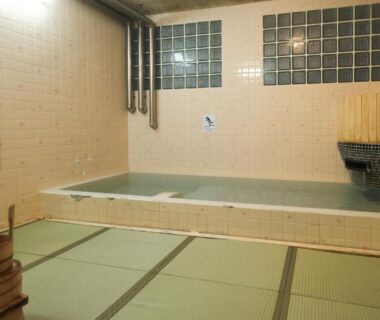 Tiled indoor bath with tatami seating area and wooden bucket at Yakuōin near Zenkoji, Nagano