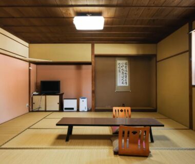 Traditional tatami room with low table, zaisu chairs, tokonoma scroll and small entertainment console at Nagano ryokan
