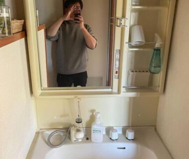 Compact bathroom sink with mirror cabinet, toiletries, and a person taking a mirror selfie at Iriyamato Nagano