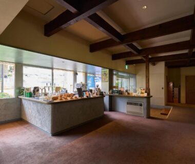 Spacious ryokan reception with merchandise counter, wooden beams and large windows at Iriyamato in Nagano Chubu