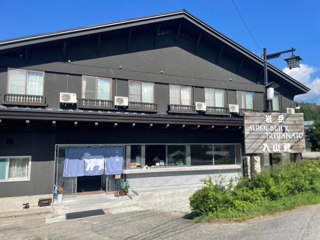 Ryokan exterior at Iriyamato in Nagano Two-story dark wooden ryokan facade with entrance, upper balconies and roadside greenery in Nagano, Chūbu