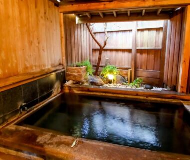Enclosed wooden bathing tub with stone edging and fence at Manrikiya in Beppu Kannawa Onsen