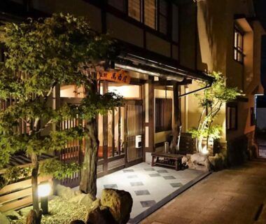 Warmly lit traditional wooden entrance with stone path and small garden at Manrikiya, Beppu Kannawa Onsen