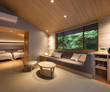 Spacious ryokan room with sofa, low table, twin beds in adjacent alcove and large window overlooking garden