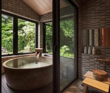 Stone soaking tub beside sliding glass doors overlooking lush garden at Hakkaisan Konohanakan, Yamanashi