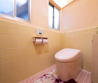 Compact toilet room with yellow tiled walls, pink mosaic floor, two windows and potted plant at Manrikiya Bekkan Beppu Kannawa