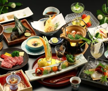 Traditional multi-course Japanese meal spread with assorted small dishes, sashimi, tempura, grilled items and decorative garnishes