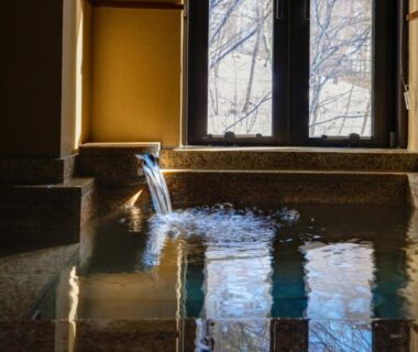 Water flowing into indoor stone onsen bath beside window with wooded view at Bettei Tateshina Kunpū, Nagano