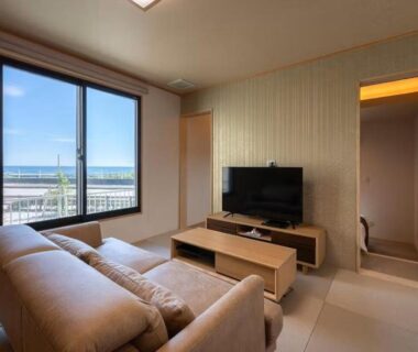 Tatami room with sofa, low table and TV at Kappō Ryokan Kiyoto in Chiba, sea visible through window
