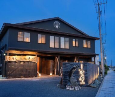 Lit exterior of two-story Kappō Ryokan Kiyoto with wooden facade and stone lantern at dusk, Chiba