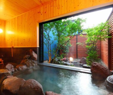 Wood-paneled indoor onsen opening to a small enclosed garden with natural stones at Shōsei no Yado Shinan, Ōita