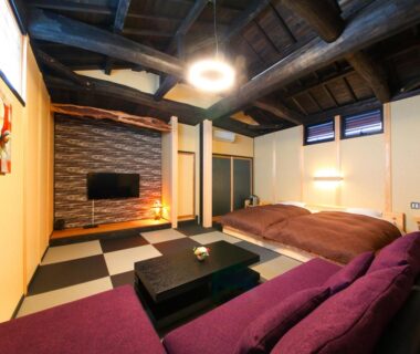 Tatami room with low table, futon beds, purple sofa and wooden beams at Shōsei no Yado Shinan, Ōita