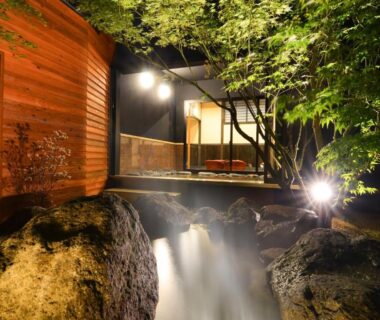 Lantern-lit wooden outdoor onsen beside rocky stream at Shōsei no Yado Shinan, Ōita