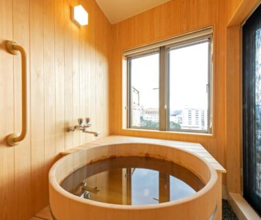 Round wooden soaking tub by window with handrail and tap at Kachōfūgetsu in Wakayama