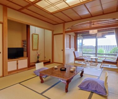 Traditional tatami room with low table, floor cushions, sliding doors and a bright seating area opening to balcony and greenery