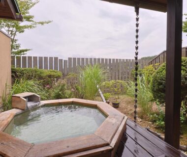Octagonal wooden soaking tub on deck overlooking an enclosed garden with rain chain, ryokan in Nagano