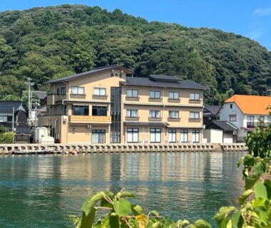 Three-story ryokan by calm waterfront, Ryokan Sakamotoya with wooded hillside backdrop in Kyoto, Kansai