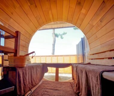 Wooden barrel sauna interior with bench seating and round window overlooking tree at Ryokan Ōmasa in Saga