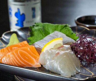 Salmon and white fish sashimi with lemon and seaweed garnishes, sake bottle in background at Ryokan Ōmasa, Saga