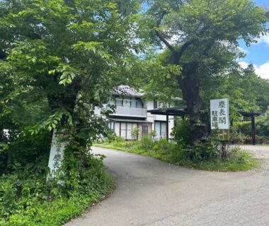 Driveway and entrance sign for Jinpyōkaku Honten amid green trees in Nagano