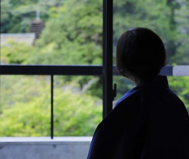 Silhouette of a guest looking through a room window at lush green hillside from Hôtel touristique Tōnomine, Nara