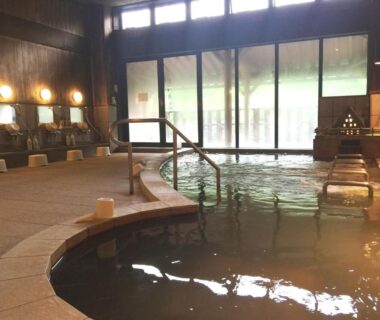 Indoor onsen bath with stone edge, wash stations and wooden stools at Shirakawagō no Yu, Gifu, Chūbu
