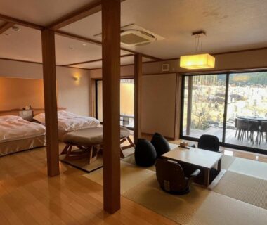 Spacious tatami area with low table and western twin beds opening to balcony at Sansō Hanayu in Kumamoto, Kyūshū