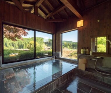 Wooden indoor onsen bath with large windows overlooking garden at Sansō Hanayu maison thermale céleste, Kumamoto