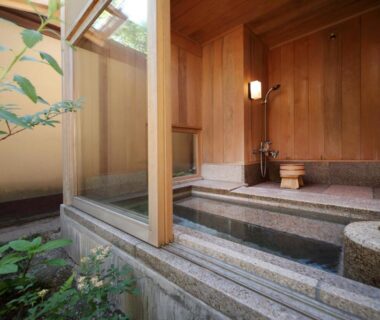 Wooden onsen bath with stone tub and glass wall opening to a small garden at TENDOSO Yamagata