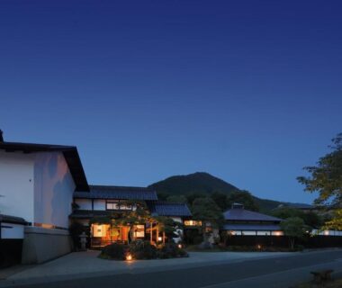 Evening view of TENDOSO ryokan exterior with lit entrance and mountain backdrop in Yamagata